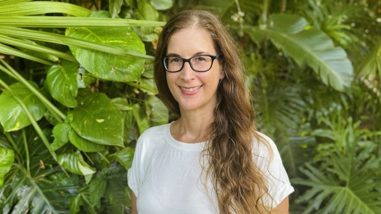 Headshot of Louise Byrne standing in front of green plants